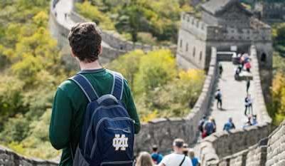 A young man wearing a blue Notre Dame backback is looking down the length of the Great Wall of China